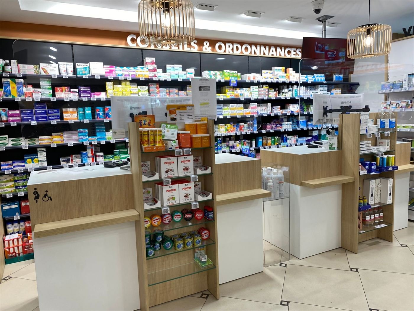 Comptoirs de pharmacie en bois et blanc, présentoirs et espace « Conseils & ordonnances »